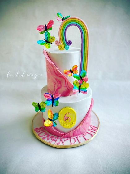 A whimsical and colorful butterfly-themed cake. The rainbow and the fluttering butterflies, all handmade from delicate wafer paper, create a sense of movement and joy.