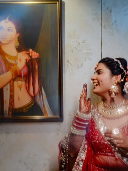 A candid moment of laughter, capturing the bride's genuine happiness as she stands beside a traditional Indian painting.
