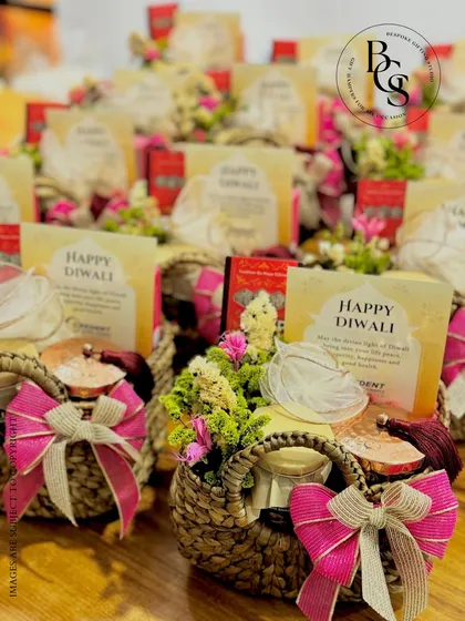 A collection of festive Diwali hampers in charming woven baskets. Each basket is filled with goodies, adorned with fresh flowers, and tied with a vibrant pink bow, ready to spread joy and light during the festive season.