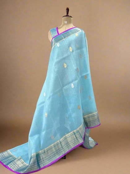 A light sky-blue pure Kora organza saree with silver butis and a contrasting purple piping border.