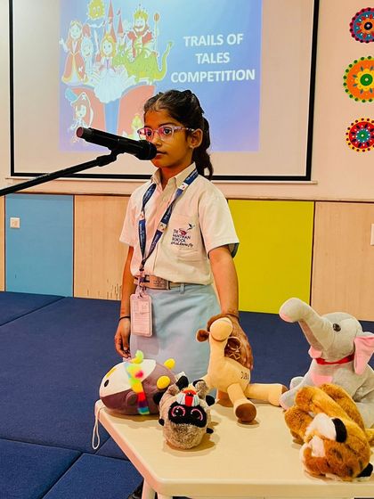 A student stands at the microphone surrounded by stuffed animal props, ready to tell her imaginative story to the judges.