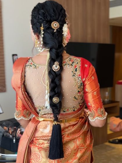 A detailed shot of a textured bridal braid adorned with traditional gold accessories and a black tassel (kunjalam) at the end.