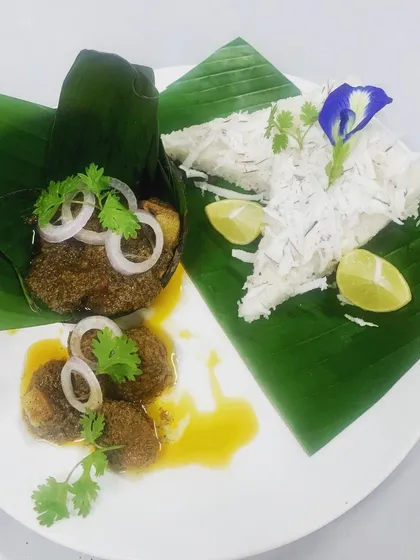 A beautifully plated breakfast of Pandi Curry and Paputtu, a traditional Coorgi steamed rice cake. Garnished with fresh onion, coriander, and a squeeze of lime, it’s a true taste of home.