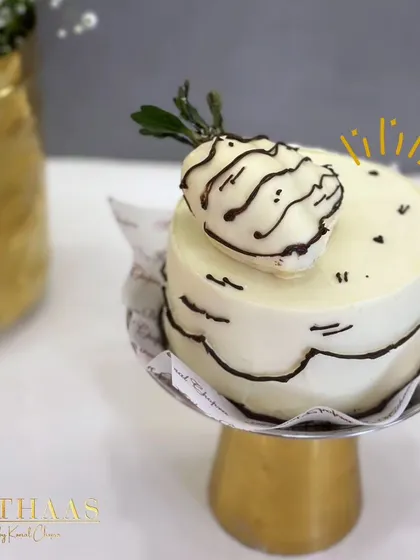 A whimsical mini-cake with a white chocolate strawberry on top. The cartoon-like black outlines give this small treat a playful and unique character.