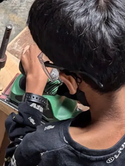 Close-up of a young maker focused on his work with a power sander. This level of concentration is a skill that translates far beyond the workshop.