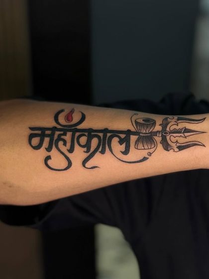 A close-up of the clean lines and bold script of a Mahakal tattoo. The details, like the third eye on the trishul, are what make it special.