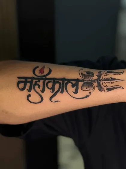 A close-up of the clean lines and bold script of a Mahakal tattoo. The details, like the third eye on the trishul, are what make it special.