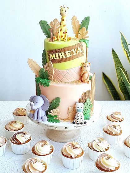 A two-tiered safari cake with matching cupcakes. The design uses a mix of 3D sculpted toppers and 2D fondant animal cutouts.