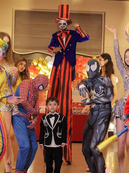 A fun group photo of the birthday boy with various entertainers, including clowns, a stilt walker, and even Spider-Man.