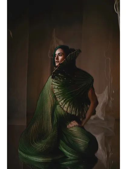 A regal, deep green gown by Vaishali S. with a massive, fan-like collar. The styling is simple and elegant, letting the garment's dramatic shape and rich color command the frame.