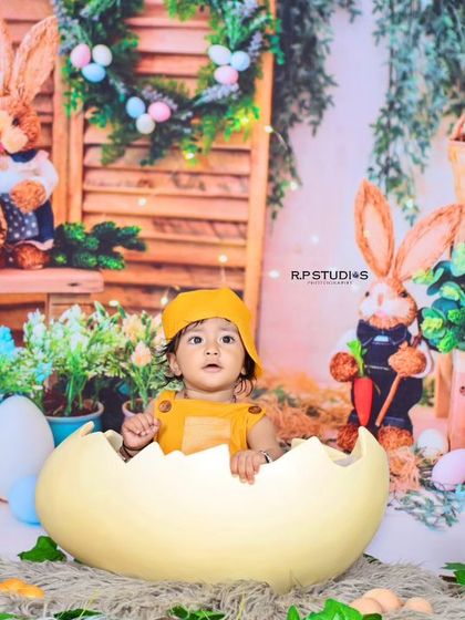 A baby hatches from a giant egg in a delightful bunny-themed Easter or spring photoshoot. The backdrop is filled with rustic charm, including bunnies, flowers, and colorful eggs.