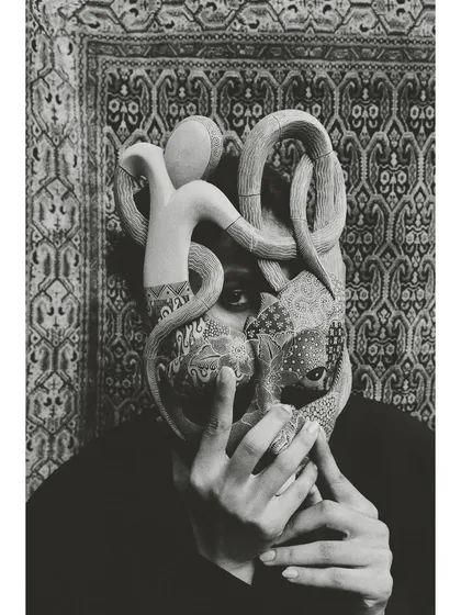 The same concept as the previous shot, rendered in dramatic black and white. The monochrome treatment emphasizes the texture of the mask and the intensity of the model's visible eye.
