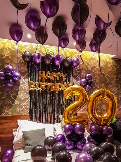 To show my range beyond traditional red, here is a stylish birthday room decoration with a modern purple and black color scheme. This surprise setup includes ceiling balloons, a foil 'Happy Birthday' banner against a black fringe backdrop, and large golden foil number balloons to mark the special age.