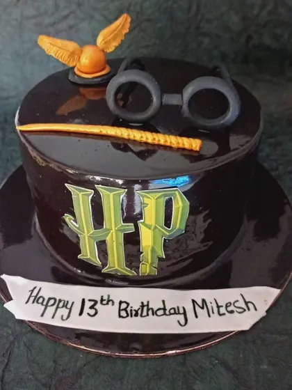 A magical Harry Potter-themed cake shaped like a hat. It's topped with the golden snitch, Harry's glasses, and a wand, perfect for any Potterhead.
