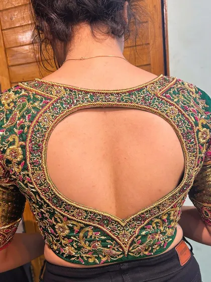 A perfect example of how a blouse can be a statement piece. This emerald green bridal blouse features a dramatic heart-shaped cutout, framed with dense zardosi and resham embroidery. The sleeves are equally detailed, making it stunning from every angle.