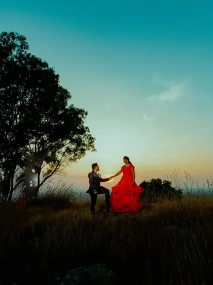 A breathtaking sunset silhouette on a hilltop. The bride's vibrant red gown flows dramatically against the twilight sky, creating a truly epic and romantic pre-wedding portrait.