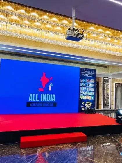 The stage for the All India Achievers Conclave. This setup features a clean, branded look with a central LED screen for presentations, a raised platform for visibility, and professional lighting to create a formal atmosphere.