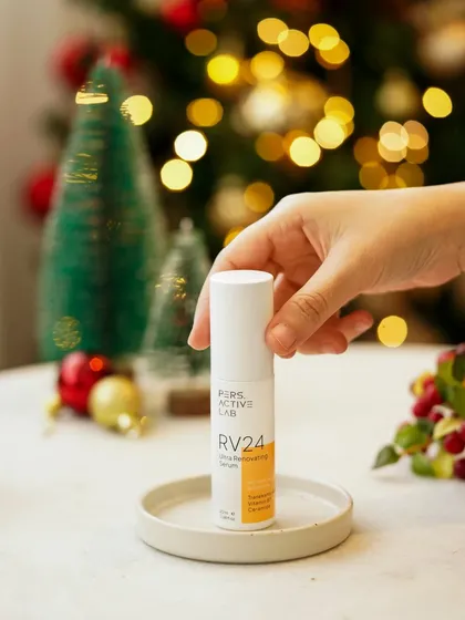 A hand holds the serum in front of a festive, bokeh-lit background. This product-focused shot uses soft, warm lighting to create a magical, celebratory mood perfect for a holiday campaign.