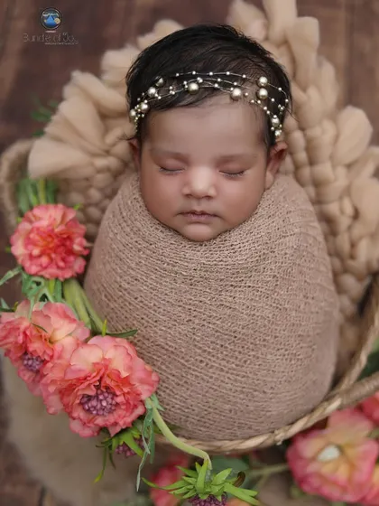 This newborn is swaddled in a soft brown wrap and placed in a basket adorned with beautiful pink flowers, showcasing a popular floral prop setup.