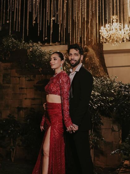 The full couple's look for a Mumbai reception. The bride's modern red outfit perfectly complements the groom's classic black suit for a chic, coordinated appearance.