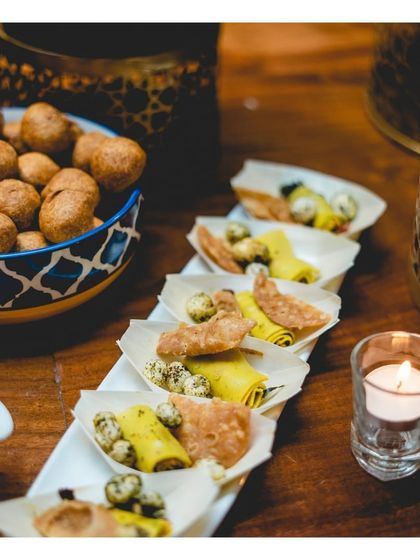 An assortment of Indian snacks, including miniature khandvi rolls and mathri, served in individual portions. This allows guests to sample a variety of traditional flavours in a refined and convenient way.