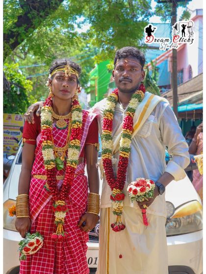 A full-length portrait of the couple just after their wedding. They are holding their flower bouquets, dressed in traditional attire, ready to greet their guests as a married couple.