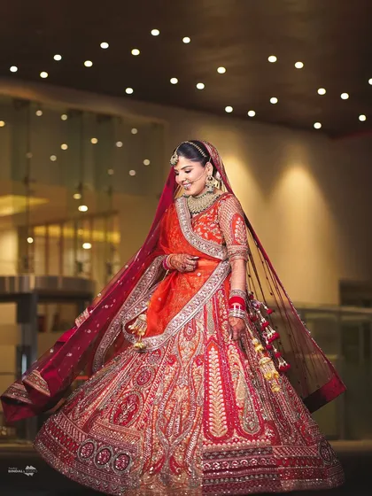 A joyful, twirling bride. This full-length portrait under a ceiling of lights captures her happiness and the beautiful movement of her orange and red lehenga.