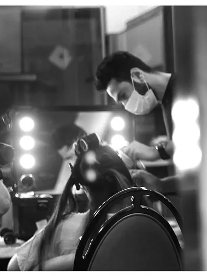 A black and white shot of our hairstylist at work in front of a professional vanity mirror. This image captures the focused and professional atmosphere we create on-site.