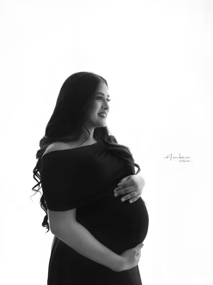 A candid, smiling close-up in black and white. This portrait captures a moment of pure joy, with the off-shoulder black top adding a touch of modern elegance.