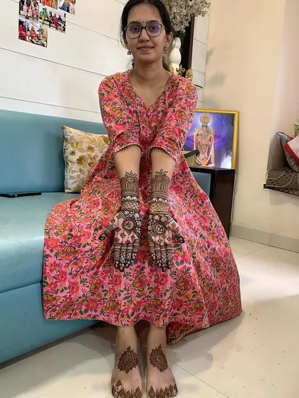 A happy client showing her complete mehndi set, including designs on her hands and feet. The foot design is a simple yet elegant mandala that matches her hand patterns.