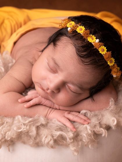 A sleeping baby girl adorned with a delicate yellow flower crown, resting on a soft, fluffy surface. A simple and sweet portrait.