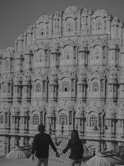 A timeless black and white photograph of the couple walking towards the Hawa Mahal. This composition emphasizes the grandeur of the architecture and the shared journey of the couple.