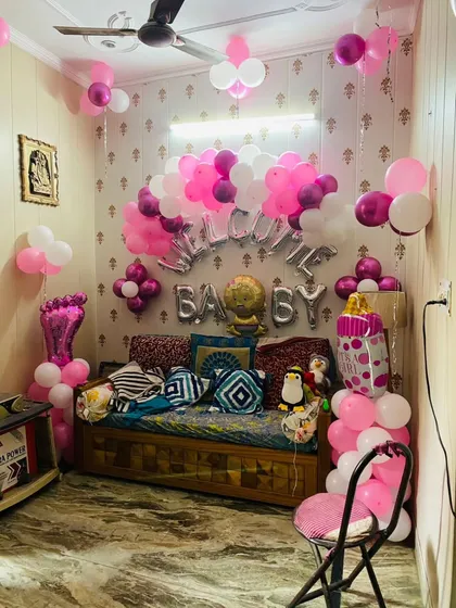 A cozy and cute welcome for a baby girl. This bedroom corner is decorated with "Welcome Baby" foil balloons, balloon columns shaped like a baby foot and a feeding bottle, and lots of pink and white balloons.