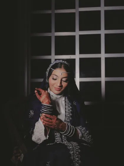 This portrait captures the bride's serene beauty just before her Nikkah. The window light creates a gentle glow, emphasizing the delicate embroidery on her dress and the traditional matha patti.