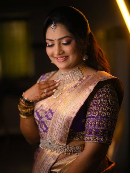 A bride in a stunning purple and gold saree, paired with a heavily embroidered blouse. The diamond jewelry adds a touch of modern glamour to the traditional look.