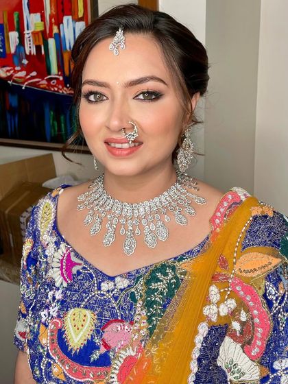 A vibrant and colorful look for a Baraat. The makeup is glamorous with a defined smokey eye and a neutral lip to balance her multi-colored lehenga.