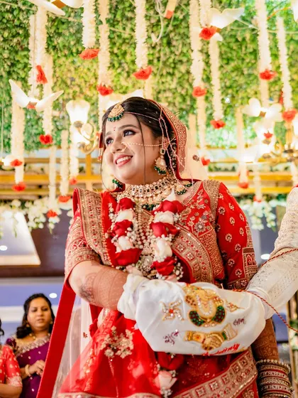 The bride's joyful smile during the Pheras ceremony. Dressed in a stunning red lehenga and surrounded by floral decor, this image captures the happiness and sanctity of the moment.