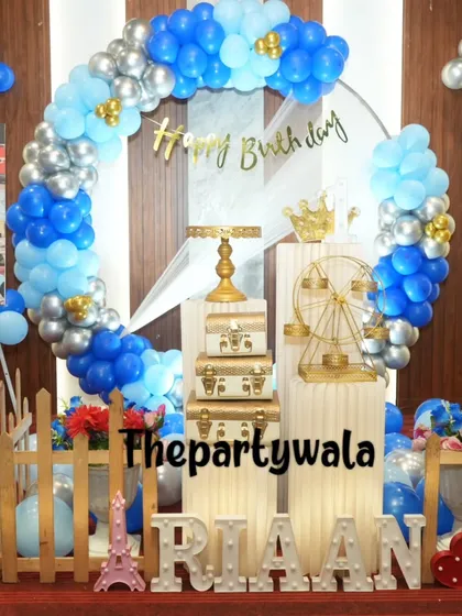 A classic blue and silver balloon ring, perfect for a boy's birthday party. The setup includes a picket fence, light-up name, and other fun props.