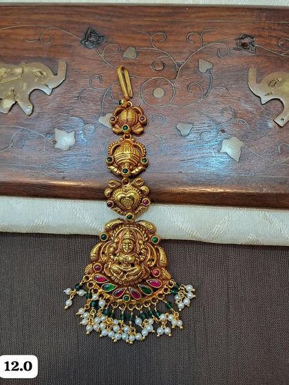 This hallmarked 92.5 silver maang tikka features a Goddess Lakshmi design. The gold plating gives it a rich look, complemented by colorful stones and pearl drops.