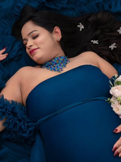 A dreamy, artistic portrait. Lying amidst a sea of deep blue fabric, this mother-to-be looks serene, with delicate flowers in her hair. This overhead shot creates a unique, painterly effect for a fine art pregnancy portrait.