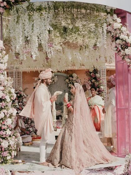 The Varmala ceremony took place under a stunning modern mandap, adorned with white, pink, and sage green florals, blending classic elegance with contemporary romance.