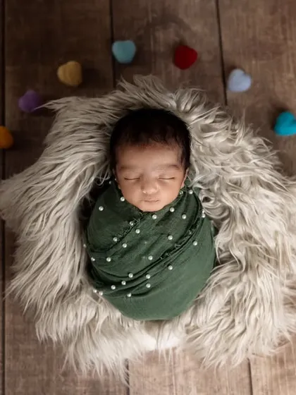 A pop of color with tiny felt hearts surrounding a sleeping newborn. The baby is wrapped in a deep green swaddle, creating a lovely contrast against the wooden backdrop.