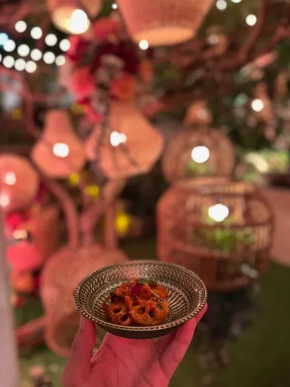 A small bowl of a flavourful appetizer, held amidst the warm, festive glow of an anniversary party's decor.