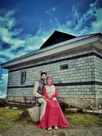 A dramatic, wide-angle shot of a couple against a traditional stone house and a vivid blue sky. I use advanced editing techniques to enhance the mood and create a powerful, cinematic image.