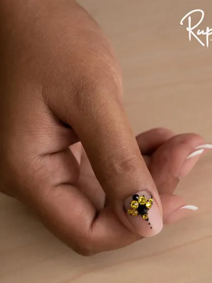 A close-up of a yellow and black crystal design on a single nail.