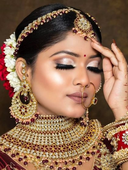 A close-up of a bride wearing a red and gold choker with a matching matha patti and large earrings. The flowers in her hair add a beautiful touch.