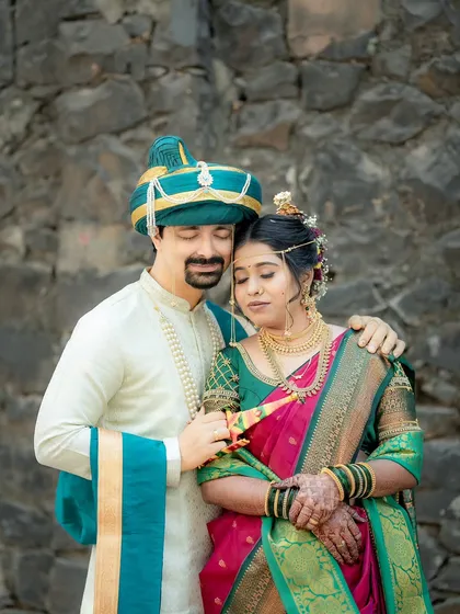 An intimate portrait of a Maharashtrian couple against a rustic stone wall, highlighting the rich colors of their traditional wedding clothes.