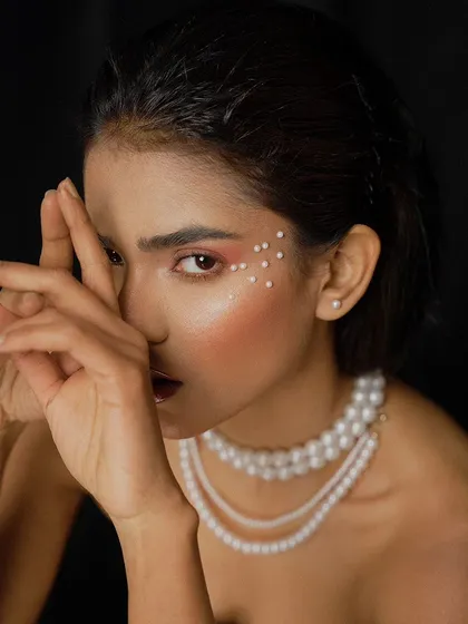 A creative beauty portrait where the model's hands frame her face. This pose adds a dynamic element and draws attention to the artistic pearl makeup.