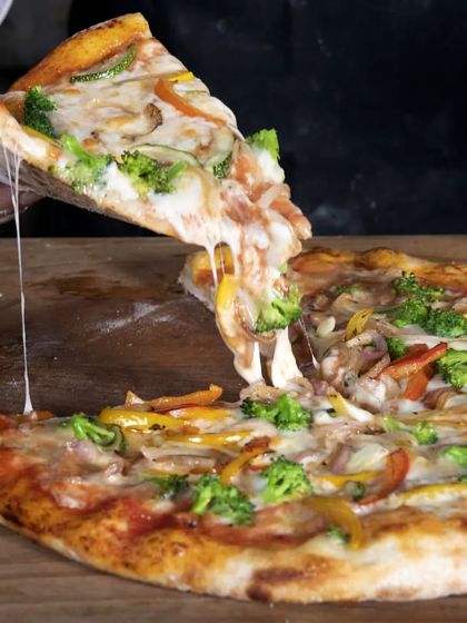 A slice of our vegetable pizza being lifted, showing the delicious melted cheese. Our pizzas are perfect for sharing and are a more casual, rustic part of our menu.