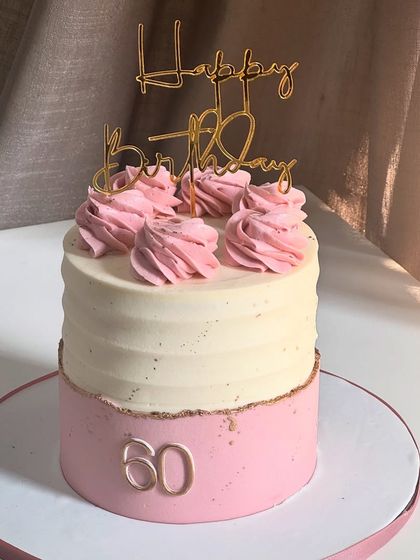 Sweet sixty never looked so good. This cake celebrates a milestone with elegance, featuring swirls of pink buttercream, a textured white top tier, and a touch of gold.